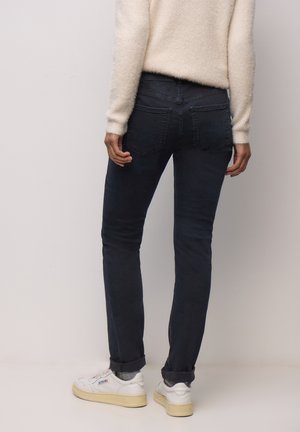 Mørkeblå denimjeans med et slankt fit, to baglommer og opsmøgede manchetter. Bærer hvide sneakers og en cremefarvet, fluffy sweater.
