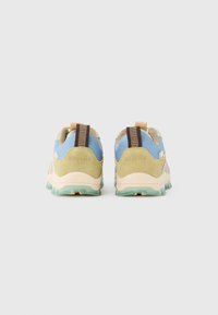 Ζευγάρι αθλητικών παπουτσιών σε μπεζ, μπλε και πράσινο χρώμα με υφή στις σόλες και ριγέ λουράκια τράβηγματος, φαίνονται από πίσω επάνω σε λευκό φόντο.