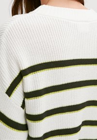 Pull en maille blanche avec des rayures horizontales en vert foncé et jaune fluo. Matériau texturé avec un col et des manches côtelés.
