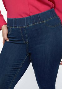 Tummansiniset jeggingsit, joissa on joustava vyötärö; ne tarjoavat sileän pinnan, huomaamatonta taskin ompelua ja vartalonmuotoisen lahkeen muotoilua.