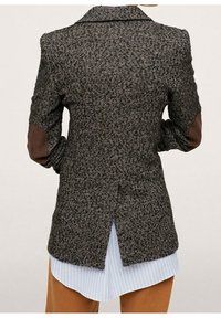 Sort og grå tweed blazer med krave, brune læderlapper på albuerne og en slids i ryggen. Laget over en lyseblå, stribet skjorte.