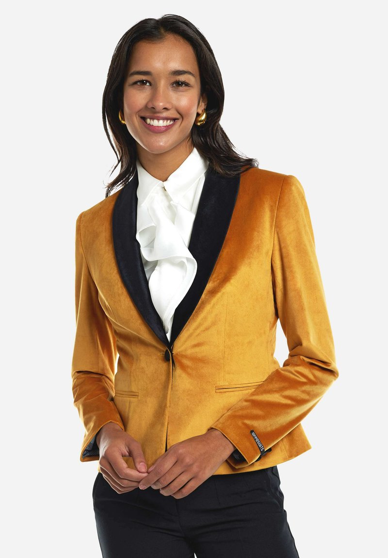 Blazer de terciopelo en mostaza con un cuello de chal de satén negro. Presenta un cierre de un solo botón y un ajuste entallado con bolsillos laterales.