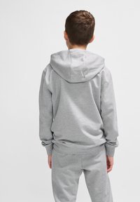 Grauer Hoodie mit lässiger Passform und Kängurutasche, aus weichem Stoff, mit großer Kapuze und gerippten Bündchen, getragen mit passenden Hosen.