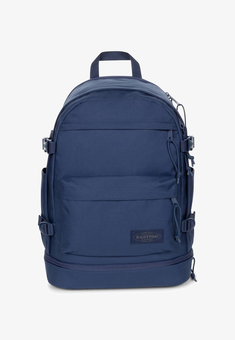 Mochila azul marino hecha de tela duradera, con correas ajustables, bolsillo frontal con cremallera y parche con logotipo. Textura suave, diseño redondeado.