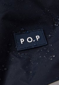 Navy vedenne kova, joka esittelee kohotetun "P.O.P" -brändäyksen tekstuuripatchissa, ja pinnalla on näkyviä pisaroita.