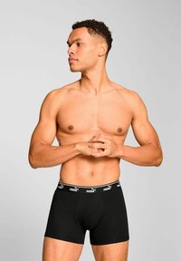 Black cotton boxer briefs with a fitted design, featuring a black elastic waistband with white "PUMA" branding. Model poses sideways.