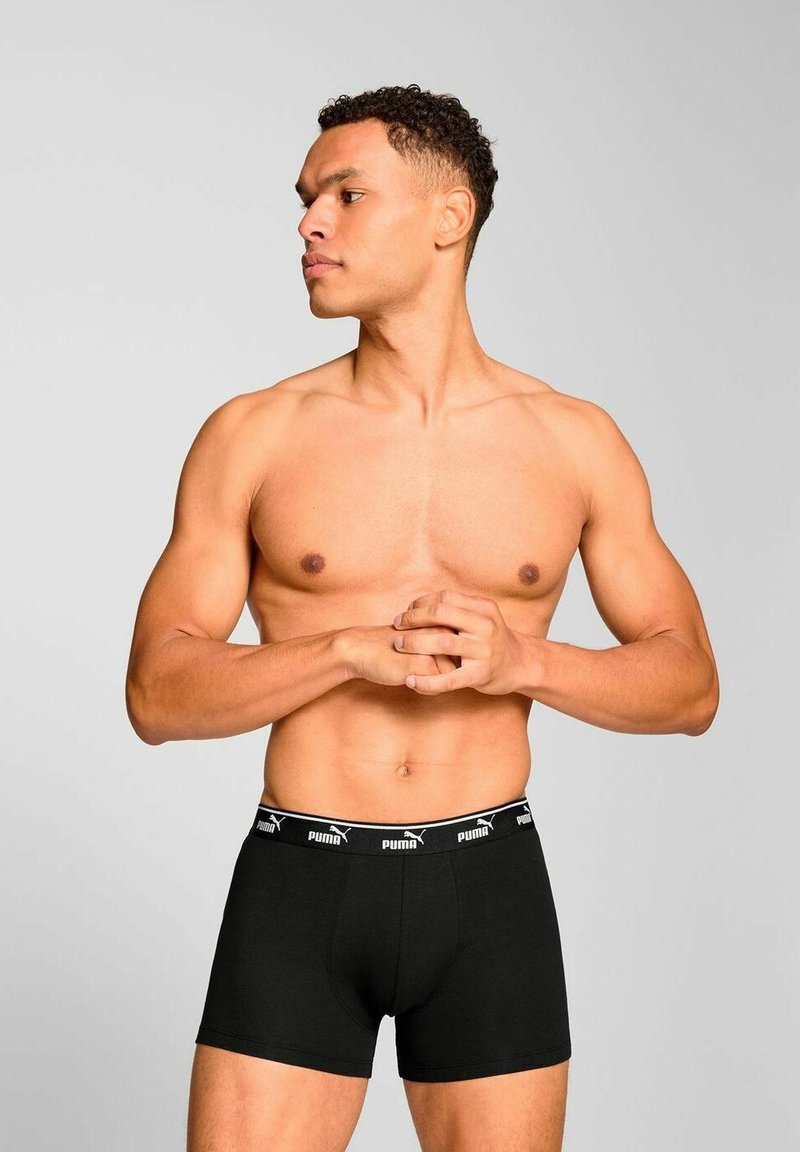 Black cotton boxer briefs with a fitted design, featuring a black elastic waistband with white "PUMA" branding. Model poses sideways.