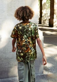 Kurzärmeliges Hemd mit einem lebhaften Dschungel-Print in Grün und Orange, aus einem weichen Stoff; kombiniert mit olivgrünen Cargohosen mit Taschen.