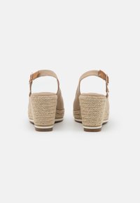 Beige wiggel sandalen met een gestructureerde geweven hak, enkelband met een metalen gesp en een gladde bovenkant, met een open achterkant.