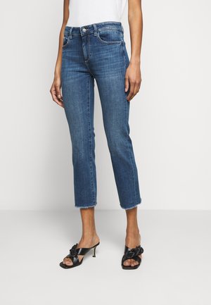 Jeans de mezclilla azul con una cintura de altura media, de longitud corta y con dobladillo deshilachado. Llevados con sandalias de tacón negro que presentan un detalle anudado.