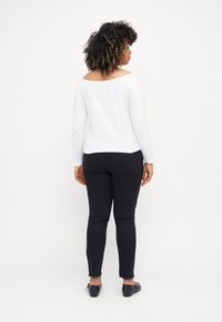 Top blanco de manga larga con diseño de hombros al descubierto, combinado con jeans negros ajustados con dobladillos deshilachados y zapatos negros tipo slip-on.