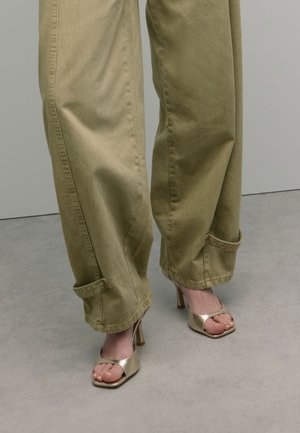 Khaki wijde broek met omgevouwen manchetten, gecombineerd met glanzende gouden open-hak schoenen, die een gladde textuur en een slank ontwerp tonen.