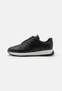 Svart lädersneakers med en slät yta, som har en vit sula, snörningsdesign och subtila sidodetaljer. Låg toppsilhuett.