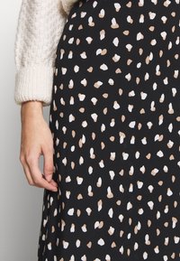Black fabric with a scattered pattern of white and beige shapes, featuring a soft texture. Part of a hand is visible, holding the skirt.