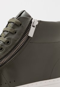 Groene leren hoge sneakers met een zijrits, tonale veters en een witte rubberen zool. Gladde textuur met contrasterende hardwaredetails.