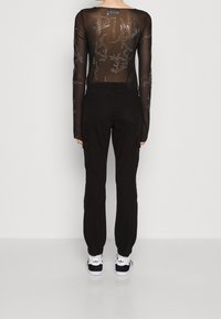 Svart genomskinlig långärmad topp med broderade mönster, tillsammans med svarta cargobyxor och vita sneakers, med elastiska ärmslut och bakfickor.