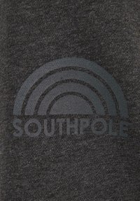 Sötétszürke szövet, amelyen egy nyomtatott mintázat látható, egy szivárványforma a "SOUTHPOLAR" szónak vastag betűkkel. Puha textúra, visszafogott minta.