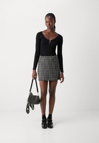 Maglietta nera a maniche lunghe a costine con dettaglio zip, abbinata a una mini gonna a righe bianche e nere. Gli accessori includono una borsa nera.