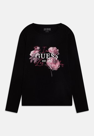 Chemise noire à manches longues avec un motif floral rose et un texte blanc et rose indiquant « Be Iconic GUESS EST. 1981 Los Angeles » sur le devant.