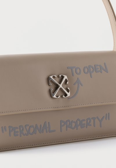 Τσάντα σε χρώμα ταουπ με ασημί πόρπη λογότυπο και γκρι χειρόγραφη επιγραφή που αναγράφει «ΓΙΑ ΝΑ ΑΝΟΙΞΕΤΕ» με βέλος και «ΠΡΟΣΩΠΙΚΗ ΠΕΡΙΟΥΣΙΑ» στο μπροστινό καπάκι.