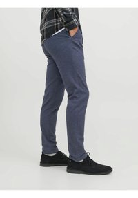 Kalhoty z tmavě modré látky s jemnou texturou, úzký střih a kapsami po stranách, doplněné černými semišovými botami.