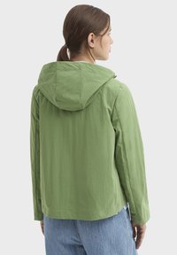 Veste légère verte avec capuche, présentant une coupe décontractée et un tissu texturé. Conçue avec des manches longues et un ourlet droit.