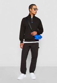 Black fleece pullover with a zip collar, paired with black cargo pants and white sneakers. A blue crossbody bag adds a pop of color.