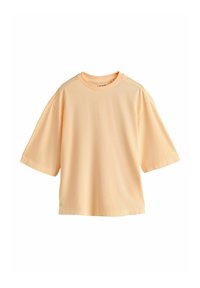 T-shirt en coton de couleur pêche clair, oversize, à manches courtes et col rond, présenté à plat sur fond blanc.