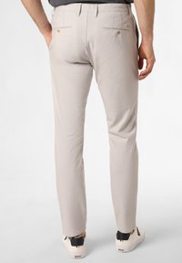 Light beige pants with a slim fit, featuring two back pockets with button closures. Worn with white sneakers and a gray shirt.