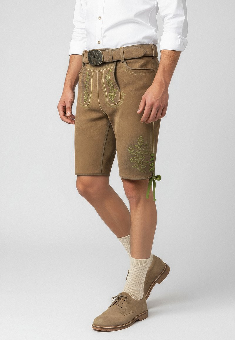 Pantaloni corti in pelle marrone con ricami verdi, dotati di tasche laterali, una cintura e lacci decorativi all'orlo, indossati con calze a coste fino al ginocchio.