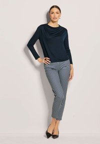 Marineblaues Langarmoberteil mit Rollkragen, kombiniert mit gemusterten Hosen mit kreisförmigen Designs in Blau und Weiß. Schwarze spitze High Heels.