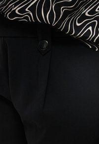 Μαύρο παντελόνι με ορατό κουμπί και ζώνη μέσης, συνδυασμένο με ύφασμα σε σχέδιο ζέβρας ασπρόμαυρο, draped πάνω από τη μέση.