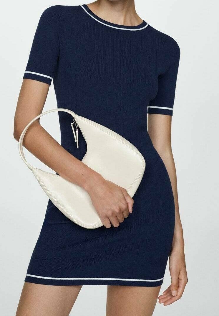 Abito aderente blu navy con rifiniture bianche sul collo e sulle maniche, abbinato a una borsa a spalla di pelle color crema a forma di mezzaluna.