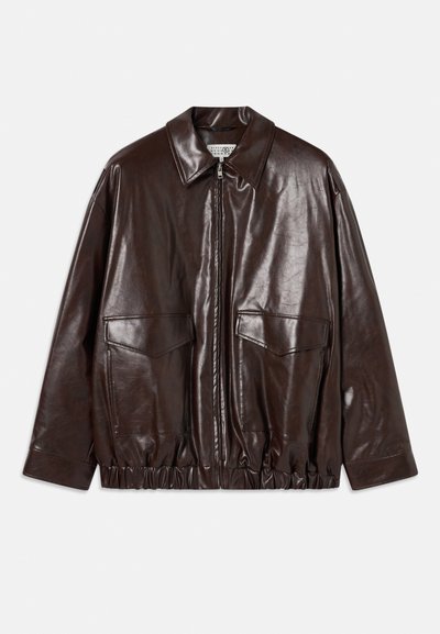 Pruun nahktagi, millel on lukuga esiosa, suured rinnakotid ja elastne vöökoht. Omab teravat kraed ja siledat tekstuuri.