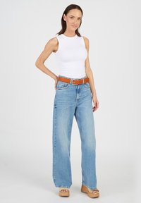 Vit ärmlös topp i kombination med ljusblå vida jeans, accentuerad med ett brunt bälte och klänning med plattformssandaler i beige. Slätt tyg med en avslappnad passform.