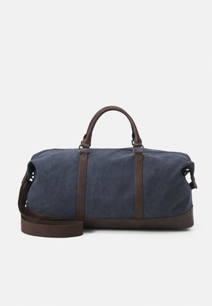 Brusttasche aus Segeltuch in Marineblau mit braunen Lederelementen, ausgestattet mit zwei oberen Griffen und einem abnehmbaren Schultergurt für vielseitige Tragmöglichkeiten.