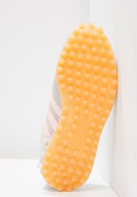 Světle šedá sportovní obuv s růžovými pruhy, vybavená texturovanou žlutou gumovou podrážkou pro optimální přilnavost.