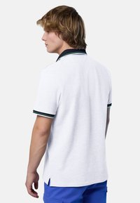 Polo shirt bianco con colletto nero e dettagli a strisce verdi e nere, dotato di maniche corte e fessure ai lati in basso.