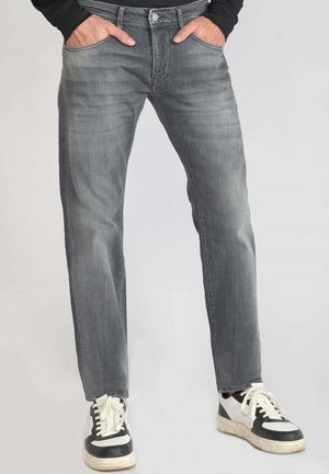 Jeans en denim gris à coupe droite, avec un design à cinq poches et des coutures visibles. Associés à des baskets noires et blanches.