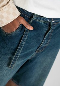 Shorts en jean d'une teinte bleu foncé, avec une poche avant dotée de coutures visibles et de fil jaune contrastant.