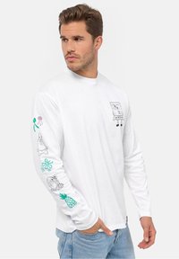 Hvid langærmet t-shirt lavet af bomuld, med legesyge sorte og farvede tryk af tegnefilmsfigurer på fronten og ærmerne.