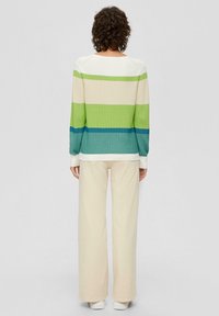 Kolorowy sweter w paski w odcieniach zieleni, niebieskiego i kremowego; struktura prążkowana, długie rękawy, okrągły dekolt, zestawiony z kremowymi spodniami o szerokich nogawkach.