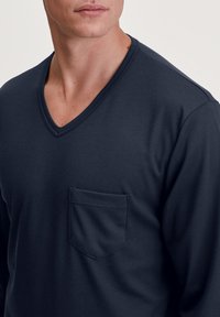 Marineblaues Langarm-V-Ausschnitt-Shirt aus weichem Stoff, mit einer Brusttasche und einem schlichten Stickdesign.