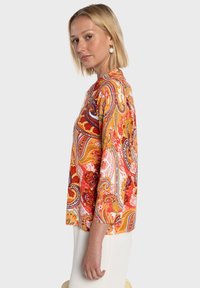 Blouse colorée à motif cachemire aux tons orange, rouge et jaune. Manches longues, tissu doux, encolure ronde et coupe décontractée.