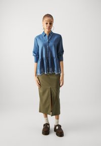 Denimskjorte med knappelukking, puffermer og brodert blondekant, sammen med et grønt midiskjørt med split foran og brune platåsko.