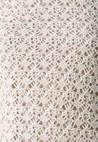 Blonde stoff i off-white, med et intrikat åpen arbeid design med gjentakende blomster- og geometriske mønstre. Myk tekstur, delikat håndverk.