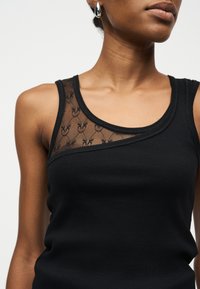 Γυναίκα με μαύρο αμάνικο τοπ με διαφανές διάτρητο σχέδιο στην πάνω αριστερή πλευρά του στήθους και ασημένια σκουλαρίκια κρίκους.