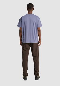 Jasnofioletowy bawełniany t-shirt z krótkim rękawem, z napisem "F.U.T." z tyłu. W komplecie z brązowymi spodniami i casualowym obuwiem.