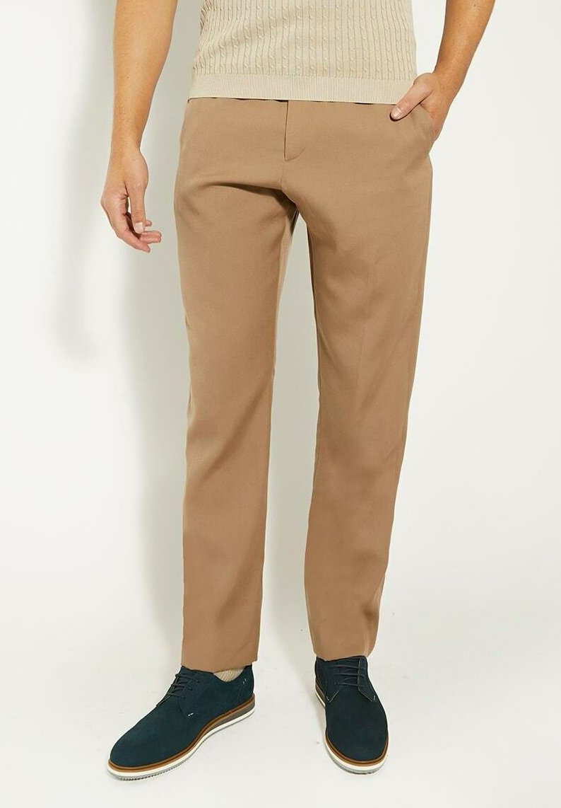 Pantalon beige à la coupe ajustée, doté de poches latérales et d'une texture lisse, associé à des chaussures bleu marine et un pull en tricot léger.
