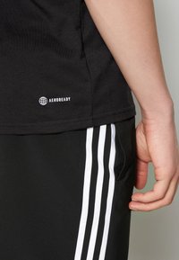 Svart AEROREADY-t-shirt med rundad nederkant, matchad med svarta byxor som har tre vertikala vita ränder längs sidan.